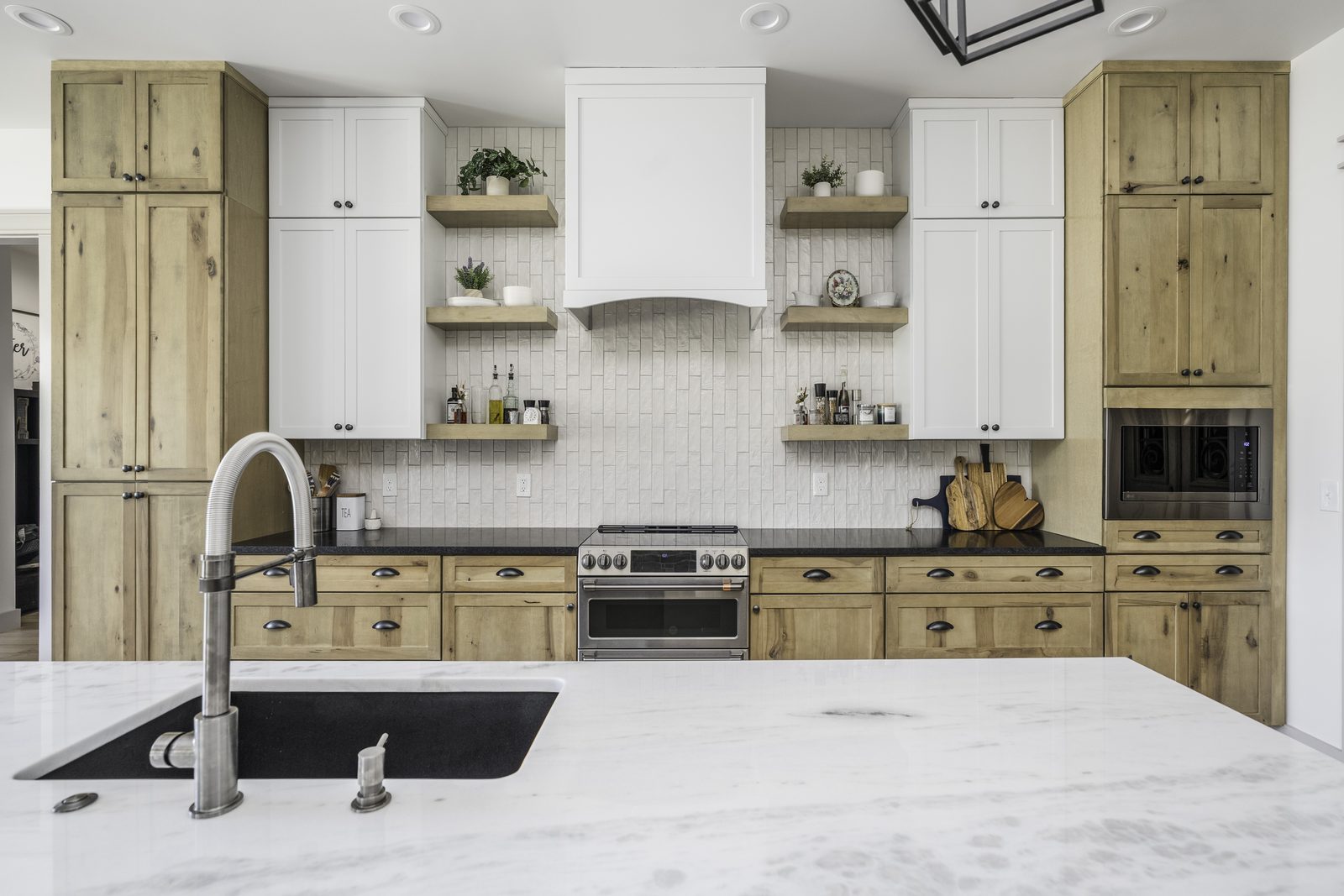 The Stone Craftsman range wall with white hood and open shelving, seen from the quartz island