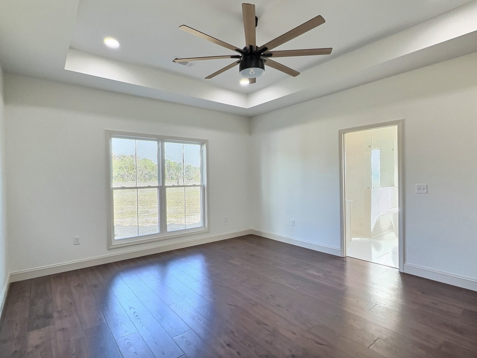 The White Farmhouse primary bedroom with tray ceiling, window and door to the bath